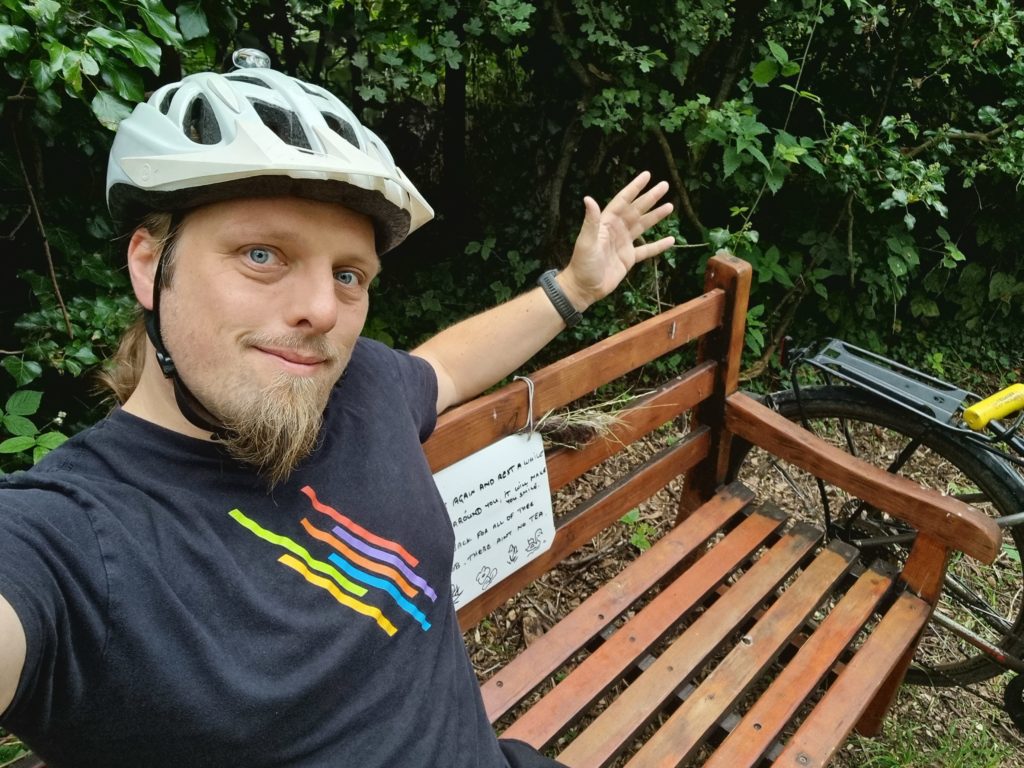 Dan wearing a cycle helmet sitting on a wooden bench.