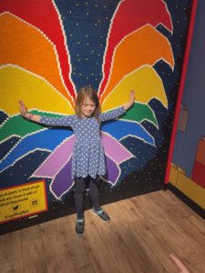Girl in front of a LEGO mosaic of butterfly wings.