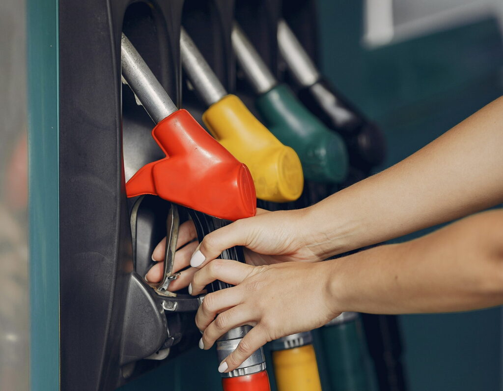 A woman's hand reaches for one of four fuel pump nozzles. Photo by Gustavo Fring, used under the Pexels License.