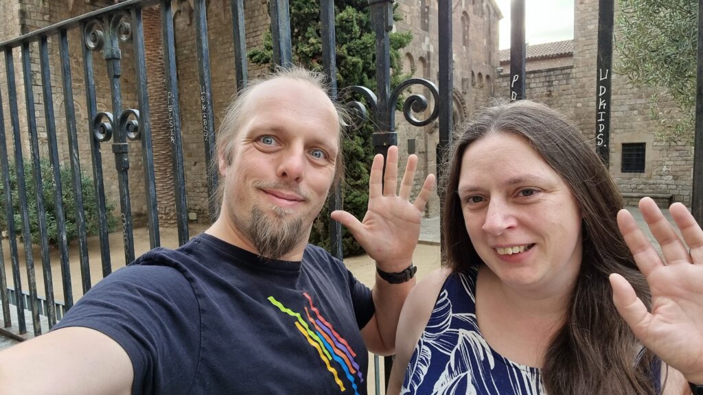 Dan and Ruth in front of a monastary gates, smiling and waving.