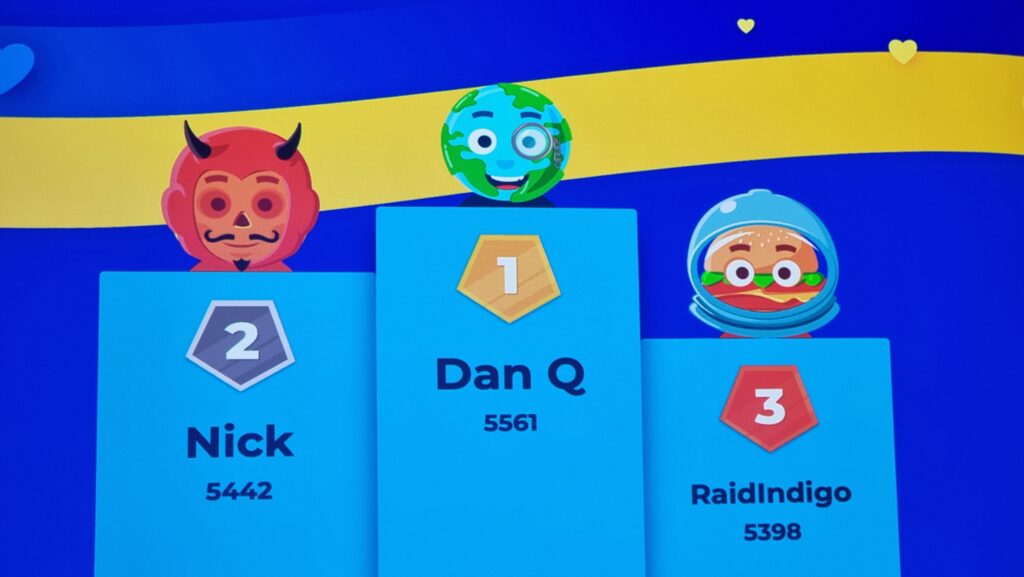 Digital scoreboard showing Dan Q in the lead with 5,561, Nick in second place with 5,442, and RaidIndigo in third with 5,398.