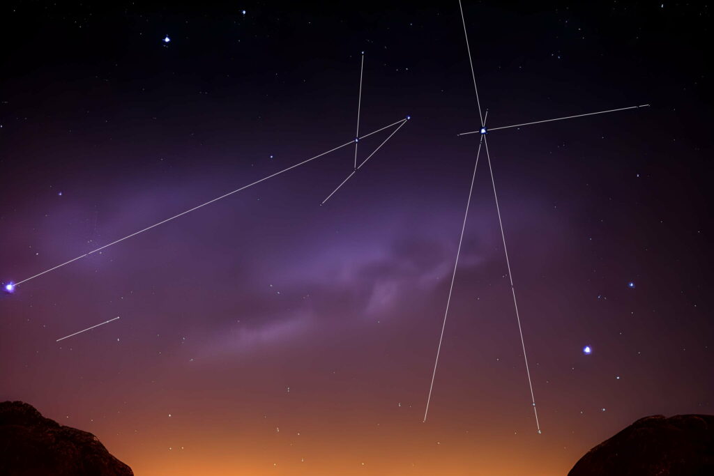 Two abstract constellations of stars drawn onto a picture of stars over the hills as the last of the sunlight begins to vanish.