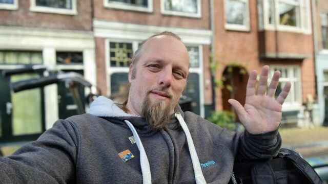 Dan, sat on a bench in Amsterdam, waves.