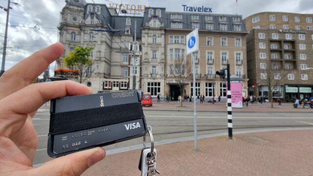 Dans fingers hold up a minimalist carbon fibre wallet in front of the Victoria Hotel in central Amsterdam. His credit card is visible showing his name but little else.