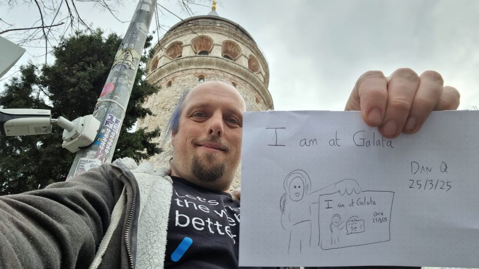 In front of the Galata Tower, Dan holds up a sign that reads 'I am at Galata' and depicts him holding up a sign that reads  'I am at Galata' and depicts him holding up a sign, and so on...