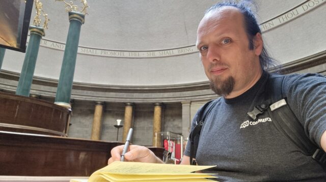 Sitting in a traditionally-decorated circular reading room, Dan writes in a notepad.
