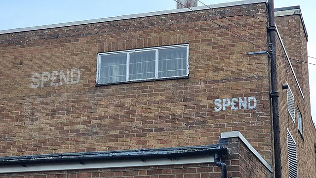 Brick building stencilled with SP£ND in two places.