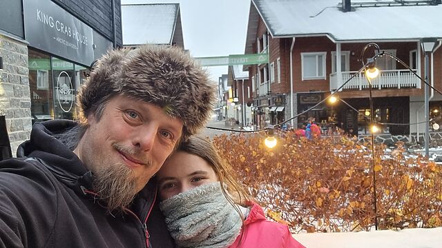 Wrapped up in warm hats and scarves, Dan and a tweenage girl stand in the snowy street of a Lapland town.