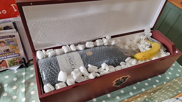 A six-litre bottle of champagne, wrapped in bubble wrap and surrounded by packing peanuts, in a wooden transport case, with a banana resting atop it.
